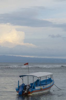 Bali, Endonezya - 17 Aralık 2024: Küçük mavi tekne suda duruyor. Gökyüzü bulutlu ve su sakin.