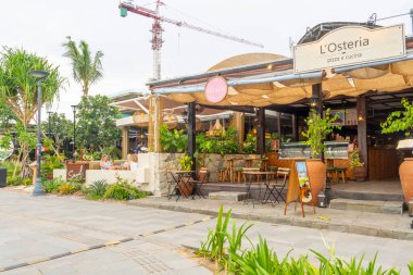 Bali, Endonezya - 17 Aralık 2024: L OSTERIA yazan bir tabelalı restoran. Dışarıda birkaç masa ve sandalye var.