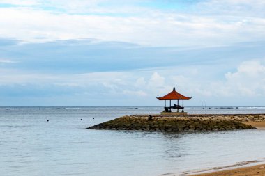 Bali, Endonezya - 17 Aralık 2024: Küçük ahşap pavyon bir plajda bulunuyor. Çadır kayalarla çevrili ve su sakin. Huzurlu ve huzurlu bir sahne.