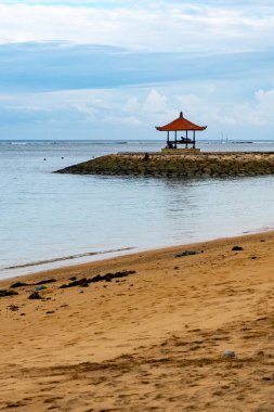 Bali, Endonezya - 17 Aralık 2024: Küçük ahşap pavyon bir plajda bulunuyor. Çadır kayalarla çevrili ve su sakin. Huzurlu ve huzurlu bir sahne.