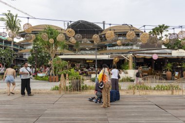 Bali, Endonezya - 17 Aralık 2024: Icon Mall Bali. Bir grup insan arka planda bir binayla parkta yürüyorlar. Manzara sakin ve huzurlu.