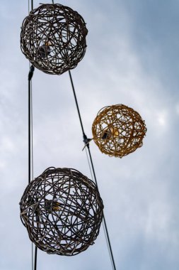 Bir kablodan sarkan üç ışıklı küre, biri sarı, biri beyaz ve biri kahverengi. Kablo bir direğe bağlı.