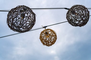 Bir kablodan sarkan üç ışıklı küre, biri sarı, biri beyaz ve biri kahverengi. Kablo bir direğe bağlı.