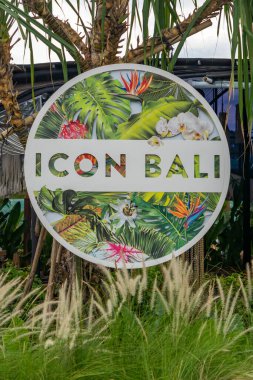 Bali, Endonezya - 17 Aralık 2024: Icon Bali Alışveriş Merkezi 'nin imzası yemyeşil bir alanda gösterildi. Tabela uzun otlar ve palmiye ağaçları ile çevrilidir. İşaret beyaz ve yeşil, tropikal bir tasarımı var.
