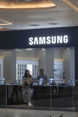 Bali, Endonezya - 17 Aralık 2024: Bali 'deki Icon Bali Alışveriş Merkezi. Tezgahın arkasında bir adam dururken Samsung mağazası. Dükkan açık ve duvarında bir saat var.