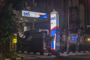 Bali, Endonezya - 17 Aralık 2024: BTN bankası geceleri aydınlanıyor. İşaret mavi ve beyaz. Banka ağaçlarla çevrili.