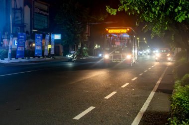 Bali, Endonezya - 17 Aralık 2024: Otobüs gece bir caddeden geçiyor. Otobüs kırmızı ve beyazdır. Sokaklar arabalar ve motosikletlerle dolu.