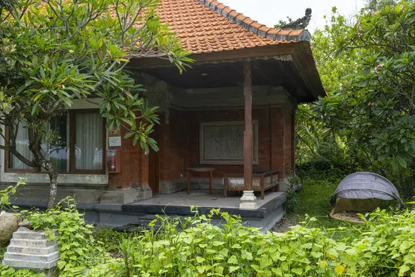 Bali, Endonezya - 17 Aralık 2024: Tahta veranda, iki sandalye ve bir bank. Sandalyeler kahverengi ve bank beyaz. Veranda ağaçlar ve çalılarla çevrili.