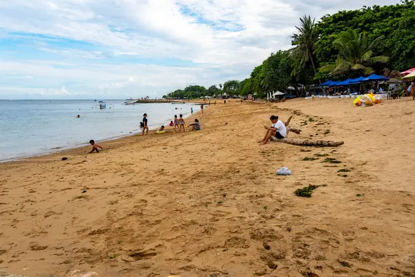 Bali, Endonezya - 17 Aralık 2024: Kumda oturup oynayan insanların olduğu plaj sahnesi. Sahne rahat ve sakin.