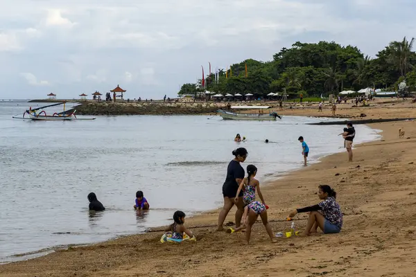 Bali, Endonezya - 17 Aralık 2024: Kumda oturup oynayan insanların olduğu plaj sahnesi. Sahne rahat ve sakin.