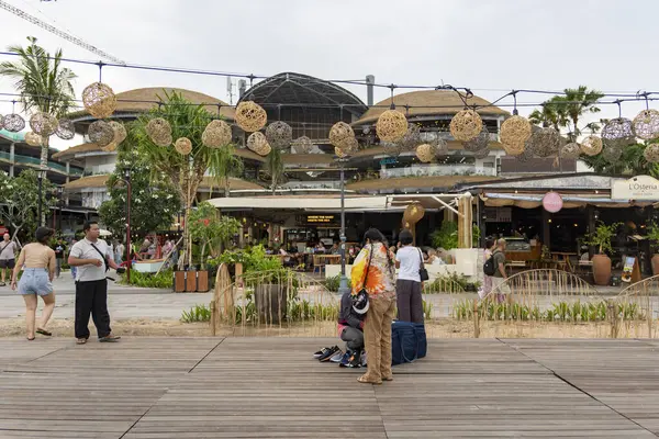 Bali, Endonezya - 17 Aralık 2024: Icon Mall Bali. Bir grup insan arka planda bir binayla parkta yürüyorlar. Manzara sakin ve huzurlu.