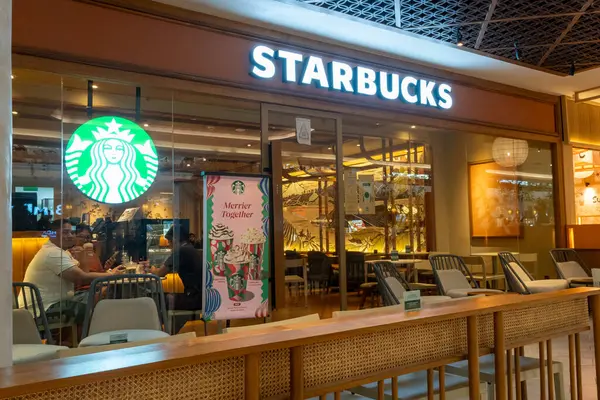 Bali, Endonezya - 17 Aralık 2024: Bali 'deki Icon Bali Alışveriş Merkezi. Starbucks mağazasının önünde bir adam oturuyor. Burası açık ve kapısında yeşil bir tabela var.