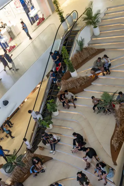Bali, Endonezya - 17 Aralık 2024: Bali 'deki Icon Bali Alışveriş Merkezi. Bir grup insan bir alışveriş merkezinin merdivenlerinde oturuyor. Alışveriş merkezi insanlarla dolu ve bir sürü merdiveni var.