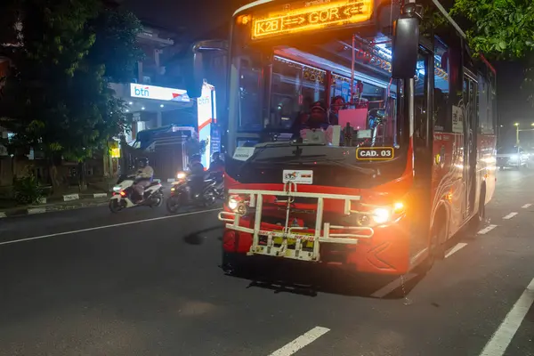 Bali, Endonezya - 17 Aralık 2024: Otobüs gece bir caddeden geçiyor. Otobüs kırmızı ve beyazdır. Sokaklar arabalar ve motosikletlerle dolu.