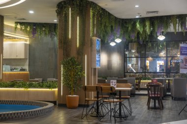 Bali, Endonezya - 17 Aralık 2024: Trans Studio Mall, Bali. Yeşil duvarı ve mavi fıskiyesi olan restoran. Birkaç masa, sandalye ve birkaç saksı bitkisi var..