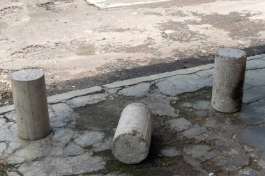 Üç çimento sütunu bir yolun önünde yerde yatıyor. Olay yeri ıssız ve terk edilmiş.
