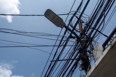 Bulutlu bir gökyüzüne karşı yıpranmış elektrik ve iletişim kablolarından oluşan kaotik bir ağ, kentsel altyapı sorunlarını vurguluyor..