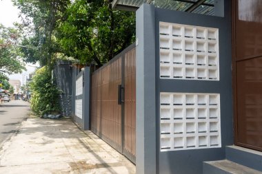 Evin önünde kapısı olan gri ve beyaz bir duvar. Kapı kapalıdır. Çit tahtadan yapılmıştır.