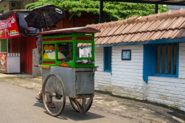 Jakarta, Endonezya - 9 Şubat 2025: Adam üzerinde şemsiye olan bir arabayı itiyor. Araba bir binanın yanındaki caddede.