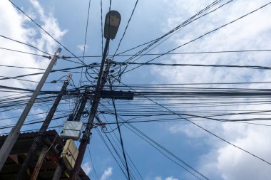 Bulutlu bir gökyüzüne karşı yıpranmış elektrik ve iletişim kablolarından oluşan kaotik bir ağ, kentsel altyapı sorunlarını vurguluyor..