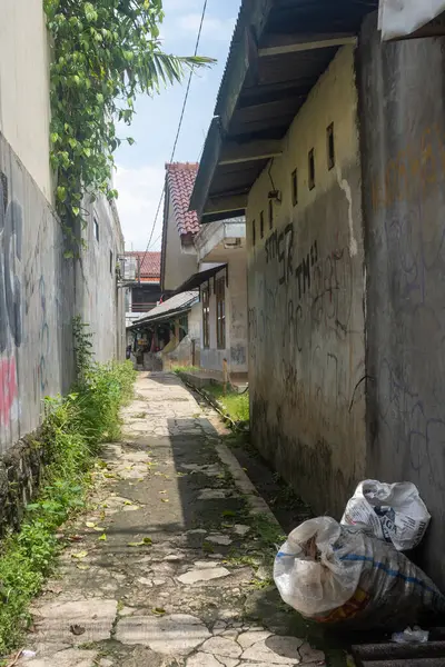 Jakarta, Endonezya - 9 Şubat 2025: Yan tarafında çöp tenekesi olan dar bir sokak. Sokak kirli ve duvarlarında grafiti var.