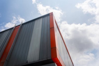 Binanın kırmızı bir çerçevesi var ve uzundur. Gökyüzü mavi ve arka planda bulutlar var.