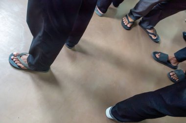 Parmak arası terlik giyen bir grup insan sırada bekliyor. Sahne rahat ve rahat.