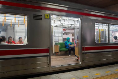 Jakarta, Endonezya - 9 Şubat 2025: Yeşil bankta oturan bir kadınla eğitim. Tren Manggarai istasyonunda. Trende başkaları da var.