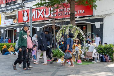 Jakarta, Endonezya - 9 Şubat 2025: Bir grup insan Mixue adında bir mağazanın önünde caddede yürüyorlar. Kaldırımda oturan birkaç kişi var. Sahne canlı ve hareketli.
