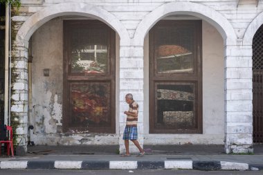 Jakarta, Endonezya - 9 Şubat 2025: Adam kemerli pencereli bir binanın önündeki caddede yürüyor.