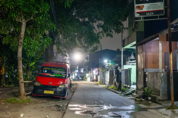 Jakarta, Endonezya - 9 Şubat 2025: Kırmızı minibüs gece bir caddenin kenarına park edilmiştir. Sokak boş ve minibüs de görünür olan tek araç.