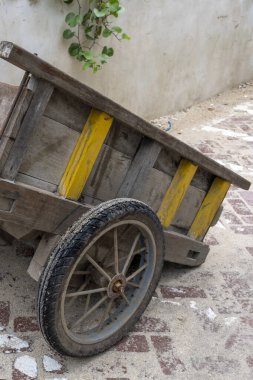 Gili Trawangan, Endonezya - 4 Ocak 2025: Sarı ve siyah tekerlekli ahşap araba duvara yaslanıyor. Araba eski ve kırsal bir görünüşü var.