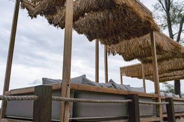 Samandan yapılmış bir gölgelik ve ahşap çerçeveli bir sahil kulübesi. Kulübe yastıklarla kaplı ve etrafında bir ip var.