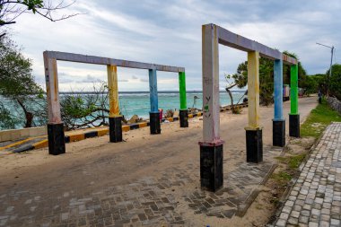 Gili Trawangan, Endonezya - 4 Ocak 2025: Okyanus kıyısındaki bir plajda renkli sütunlar duruyor. Sütunlar farklı renklere boyanmış ve bir sıraya dizilmişler..