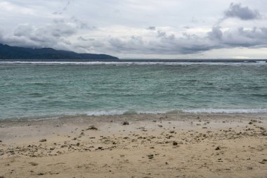 Arka planda su birikintisi olan plaj. Su sakin ve gökyüzü bulutlu.