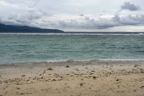 Arka planda su birikintisi olan plaj. Su sakin ve gökyüzü bulutlu.