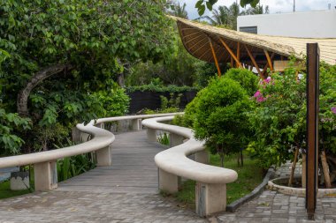 Gili Trawangan, Endonezya - 4 Ocak 2025: Bir binaya giden banklar ve ağaçlarla dolu yol. Yol banklarla kaplı ve ağaçlar yeşil.