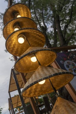 Bambudan yapılmış bir dizi ışıklı şapka. Şapkalar piramit şeklinde dizilmiş ve ışıklandırılmışlar. Sahne bir restoranda ya da benzer bir yerde geçiyor, yemek masası da var.