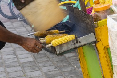 Gili Trawangan, Endonezya - 4 Ocak 2025: Adam ızgarada mısır pişiriyor. Mısır metal bir ızgarada pişiriliyor. Adam siyah bir gömlek giyiyor.