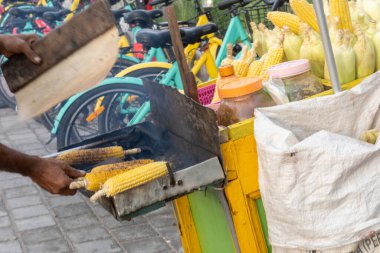 Gili Trawangan, Endonezya - 4 Ocak 2025: Adam ızgarada mısır pişiriyor. Mısır metal bir ızgarada pişiriliyor. Adam siyah bir gömlek giyiyor.