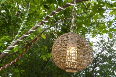 Bir ağaç dalından sarkan ışıklı fener. Fener dokuma malzemesinden yapılmıştır ve bir ampulle aydınlatılır. Sıcaklık ve samimiyet kavramı