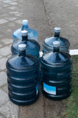 Dört büyük mavi su şişesi kaldırıma dizildi. Şişelerin hepsi aynı boyut ve şekildedir ve hepsi suyla doludur. Şişeler sıraya dizildi.