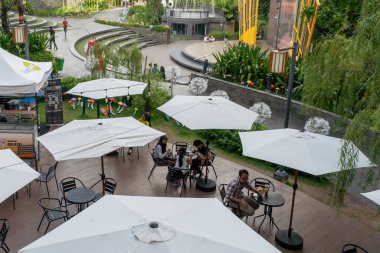 Bali, Endonezya - 23 Aralık 2024: Bir grup insan bir parkta şemsiyelerin altında masalarda oturuyor. Şemsiyeler beyaz ve onlardan çok var. İnsanlar dışarıda eğleniyor.