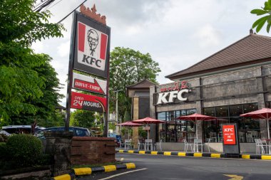 Bali, Endonezya - 23 Aralık 2024: 24 Büyük KFC restoranı. Binanın etrafı ağaçlarla çevrili ve kırmızı ve beyaz bir tabela var.