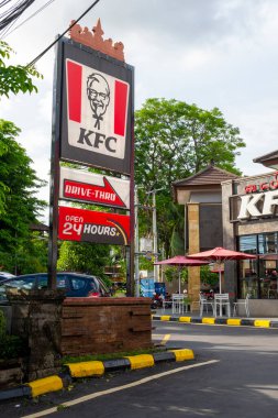Bali, Endonezya - 23 Aralık 2024: 24 Büyük KFC restoranı. Binanın etrafı ağaçlarla çevrili ve kırmızı ve beyaz bir tabela var.