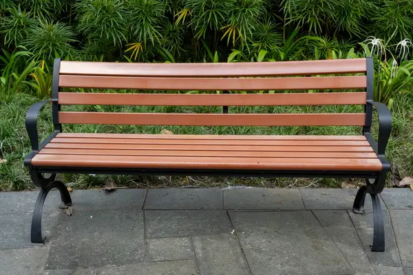 Tahta bank bir çalılığın önünde duruyor. Banklar boş, çalılar yeşil.