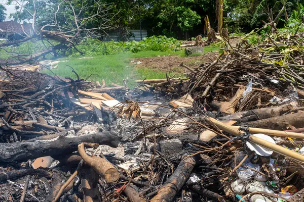 İçinden duman çıkan odun ve çöp yığını. Sahne kaotik ve dağınık.