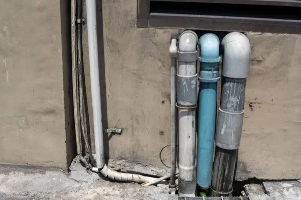 Duvarda borular var. Borular mavi ve beyaz. Duvar kirli ve borular paslanmış.