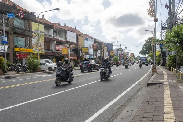 Bali, Endonezya - 23 Aralık 2024: Birçok motosiklet ve araba ile dolu cadde. Sokak binalarla dolu ve kaldırımda sarı bir çizgi var.