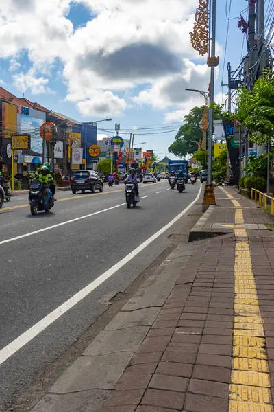Bali, Endonezya - 23 Aralık 2024: Birçok motosiklet ve araba ile dolu cadde. Sokak binalarla dolu ve kaldırımda sarı bir çizgi var.